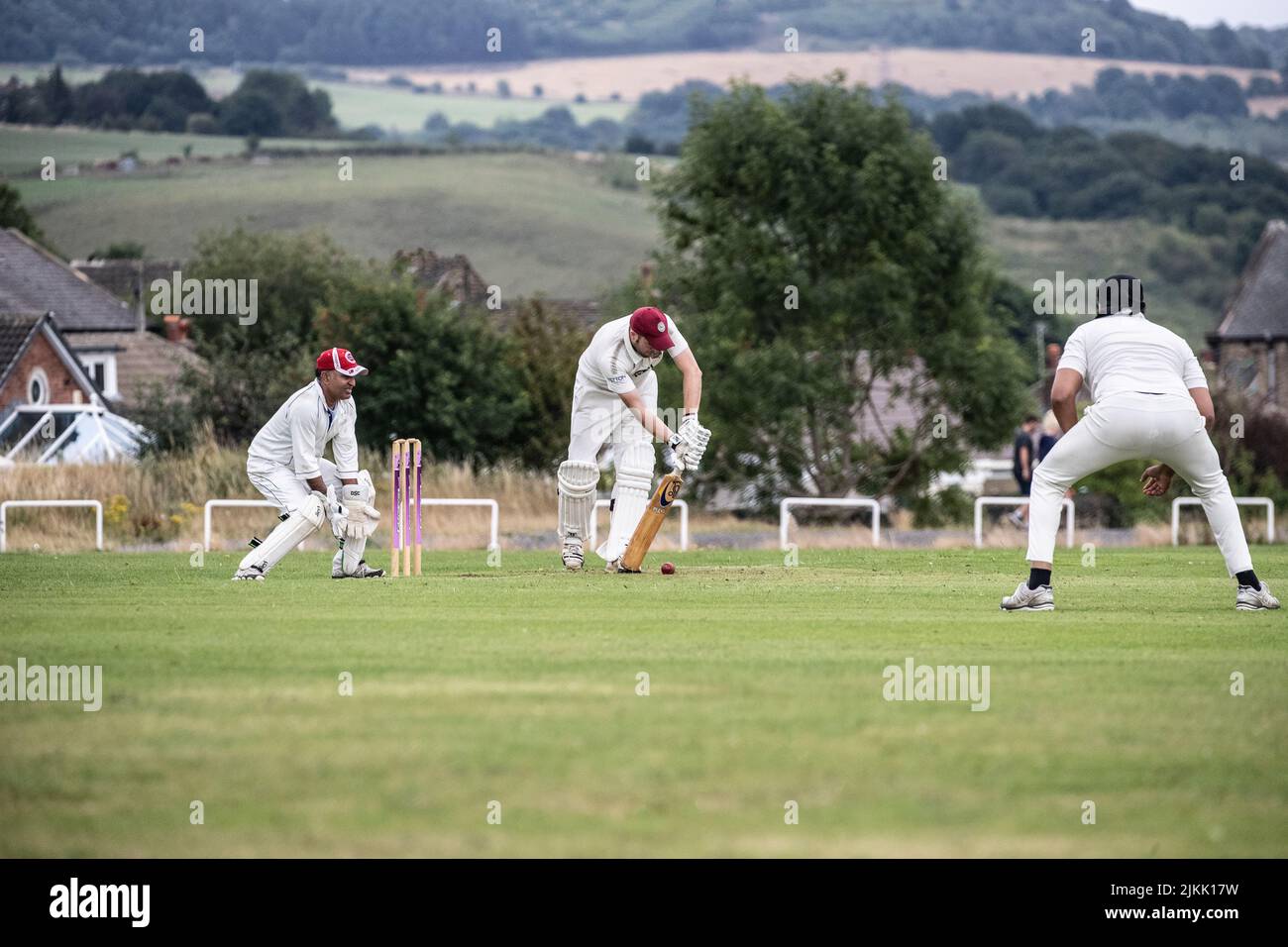 Cricket Batsman playing defensive shot watched by a wicket keeper and fielder during a weekend local village cricket match in Huddersfield, Yorkshire Stock Photo