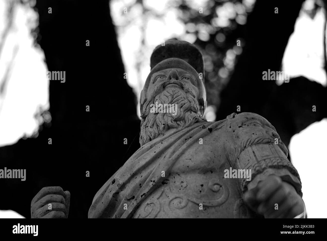 A low angle grayscale shot of the up part of a man sculpture under trees with bokeh background Stock Photo