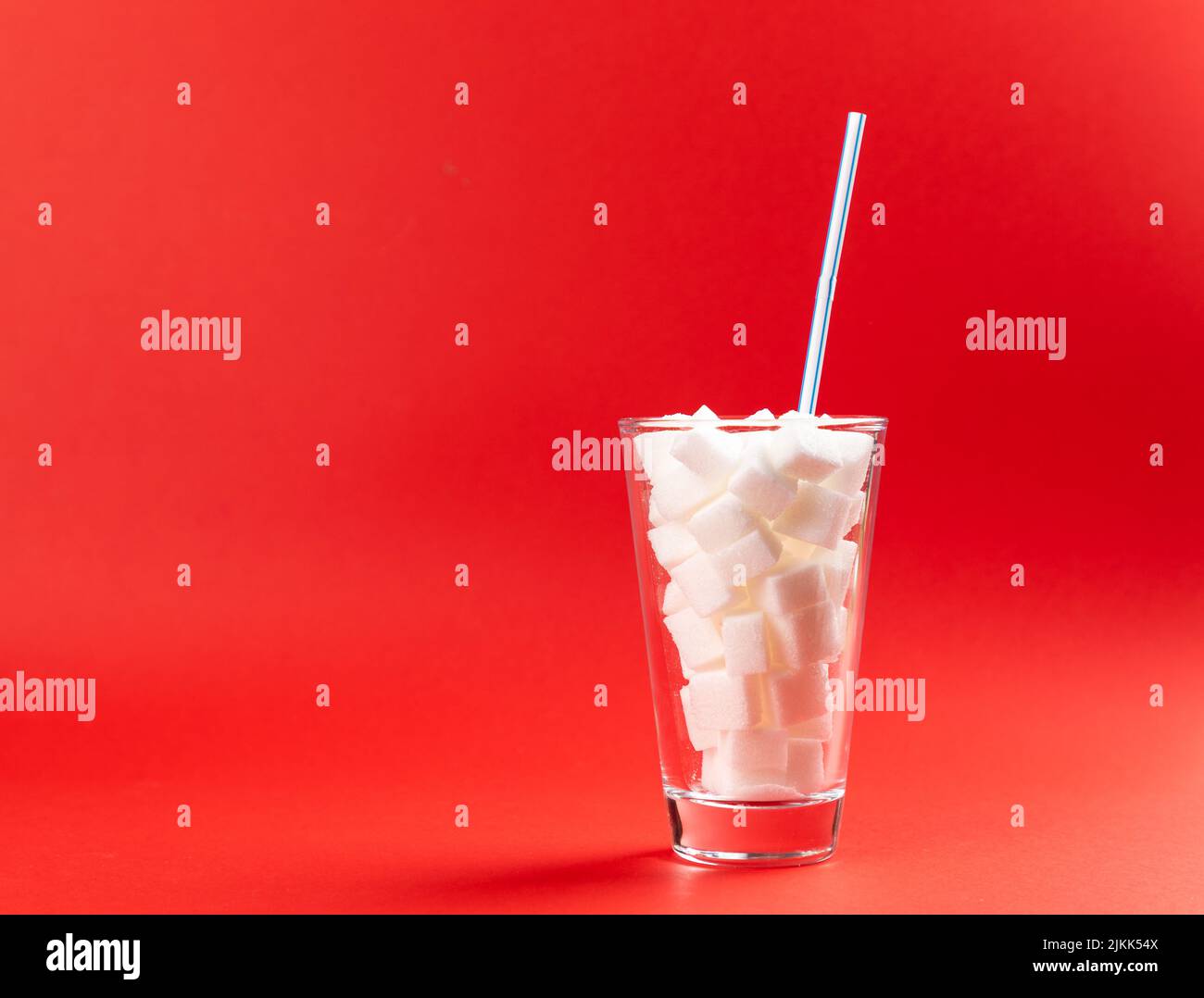 glass with sugar cubes and drinking straw on a red background Stock Photo