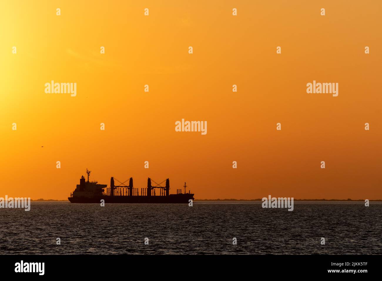 A big cargo ship, a small boat and an old pier can be seen at Uruguay River, Conchillas, Uruguay Stock Photo