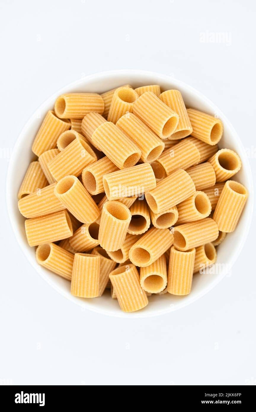 A top view of raw rigatoni pasta in a white bowl on a white background ...