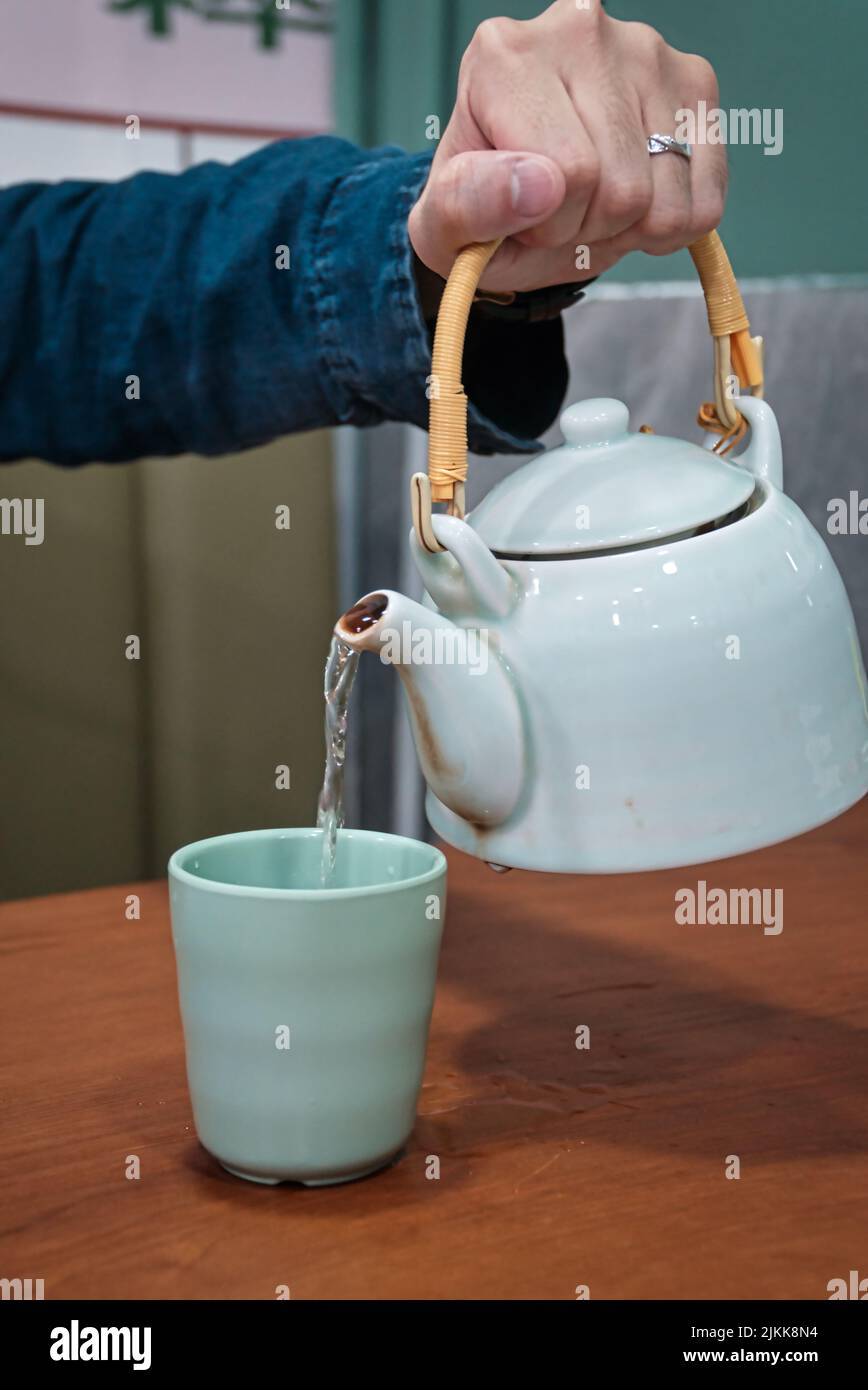 A selective focus shot of a hand pouring hot tea from a teapot to a cup