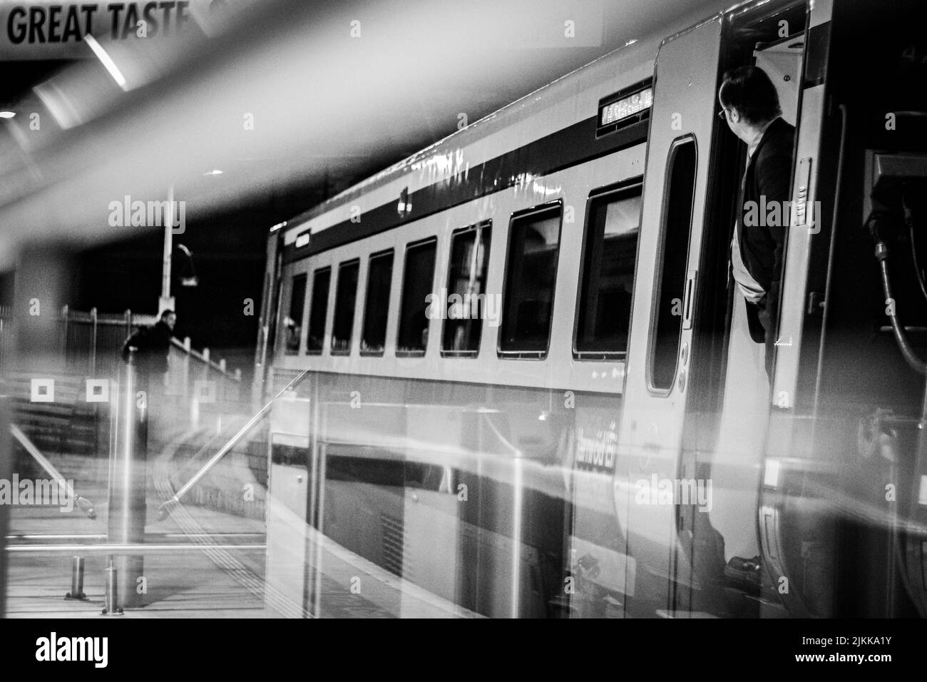 A grayscale of a man standing between doors of a train at the metro station with long exposure effect Stock Photo