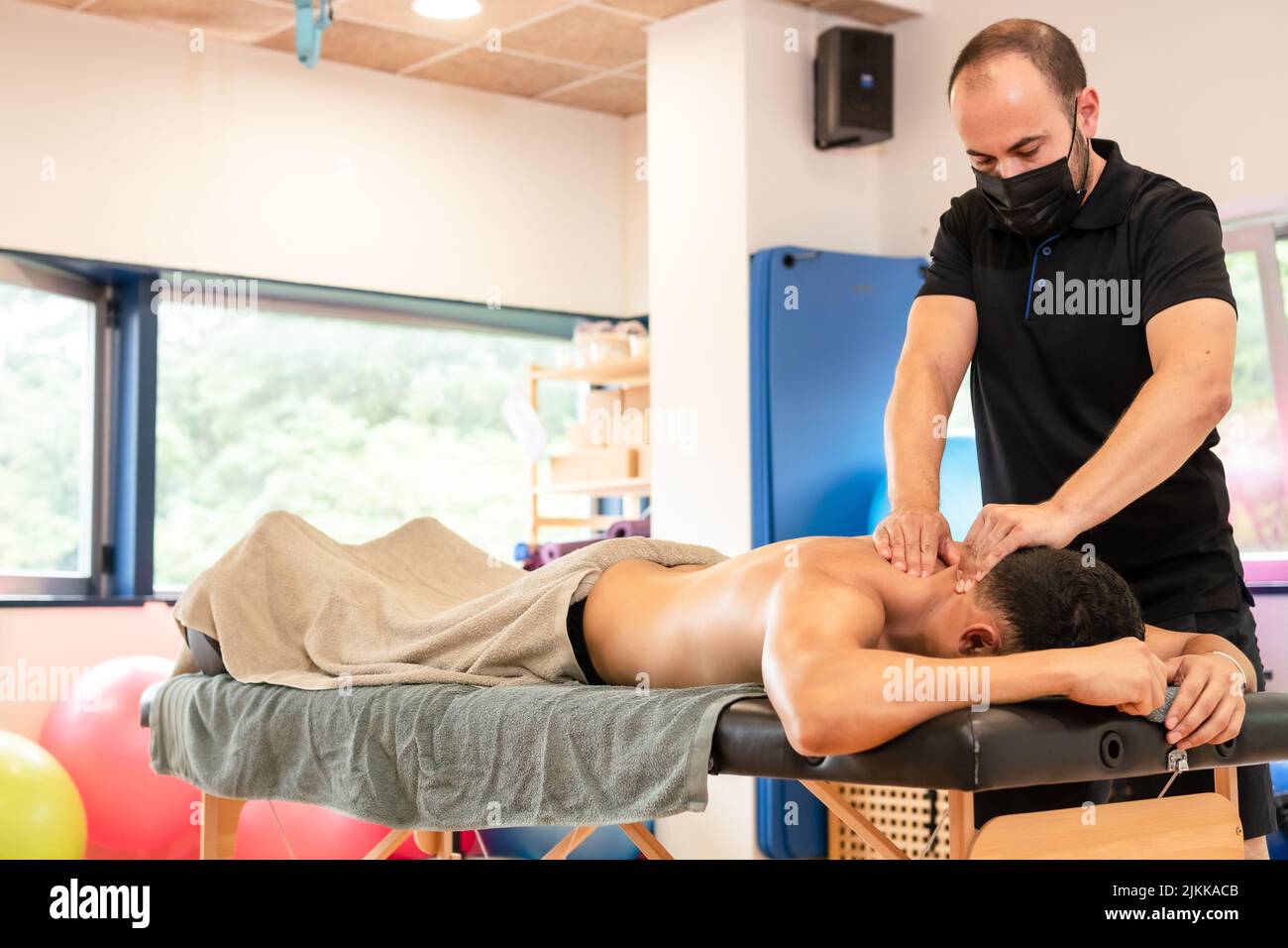 An athletic man receiving a recovery massage by a physiotherapist on a table, therapeutic back massage and osteopathy Stock Photo