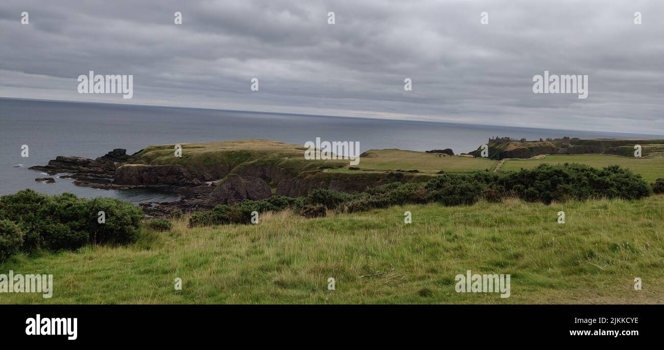 A beautiful view of green land with calm seawater on a cloudy day Stock Photo