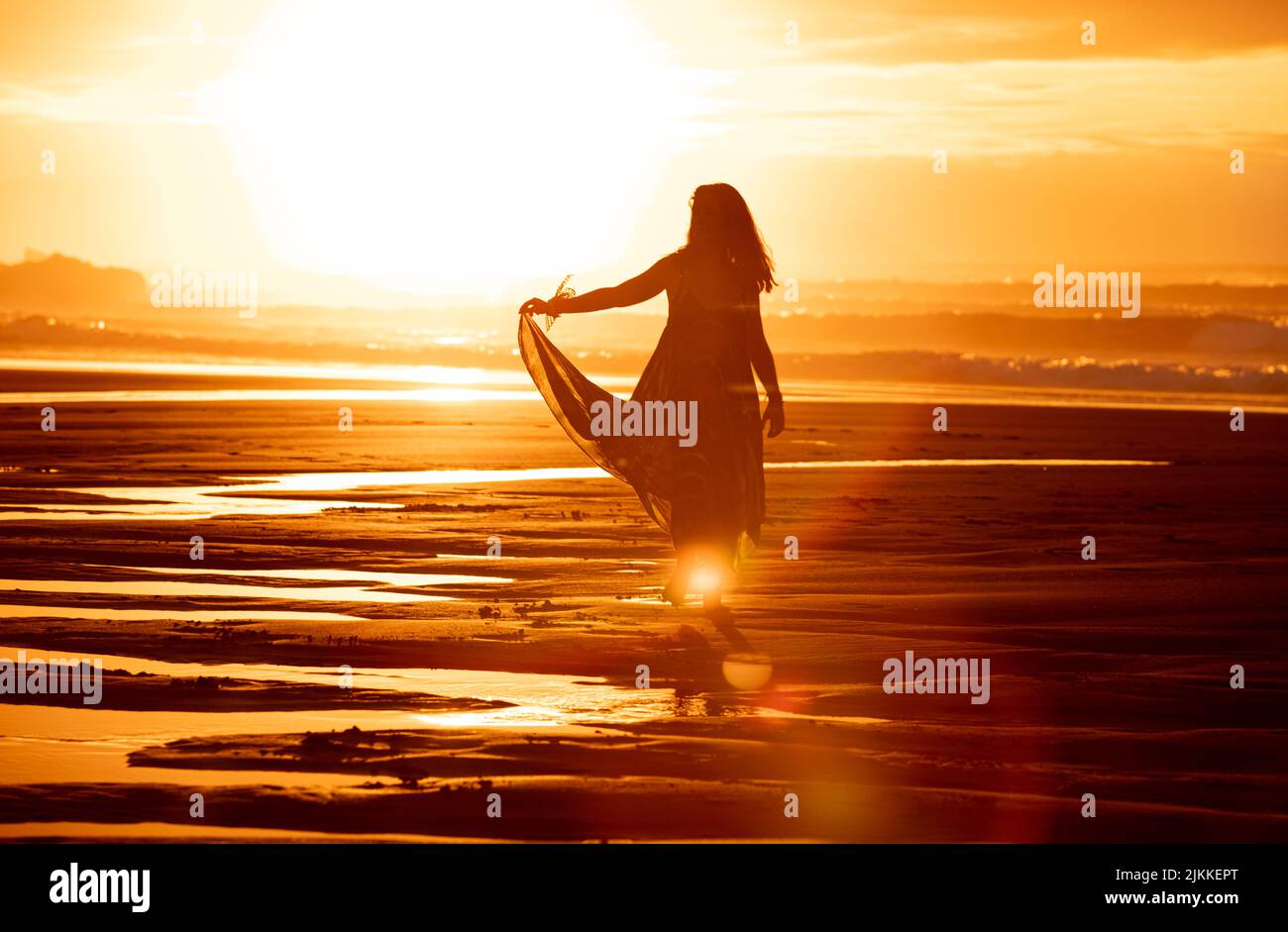 A silhouette of a female in a dress posing on a seashore at sunset ...