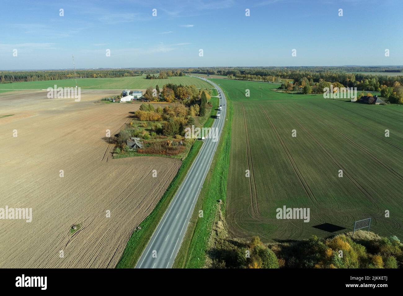 An aerial view of an asphalt road going through green fields with ...