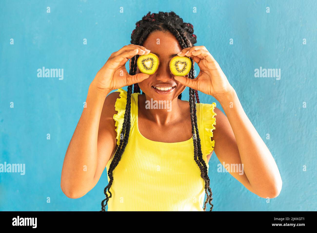 A cheerful young mixed race female holding kiwis in front of her eyes Stock Photo