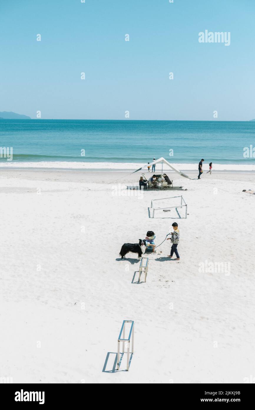 A beautiful sandy beach in Shenzhen with tourists resting and kids playing with a dog Stock Photo