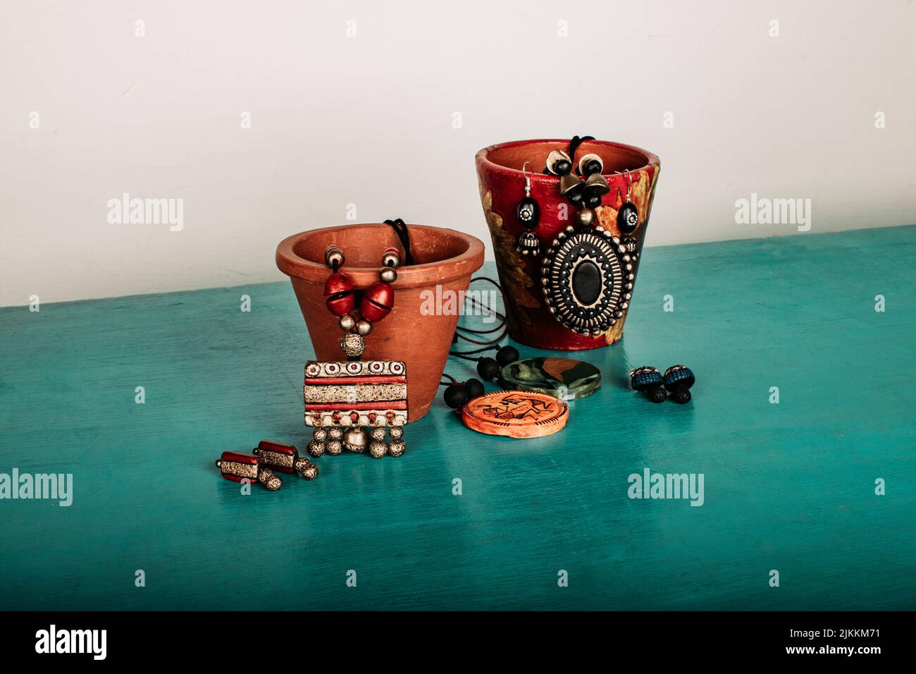 A closeup shot of traditional necklace and earring pieces set in decorated pots on a dark green table Stock Photo