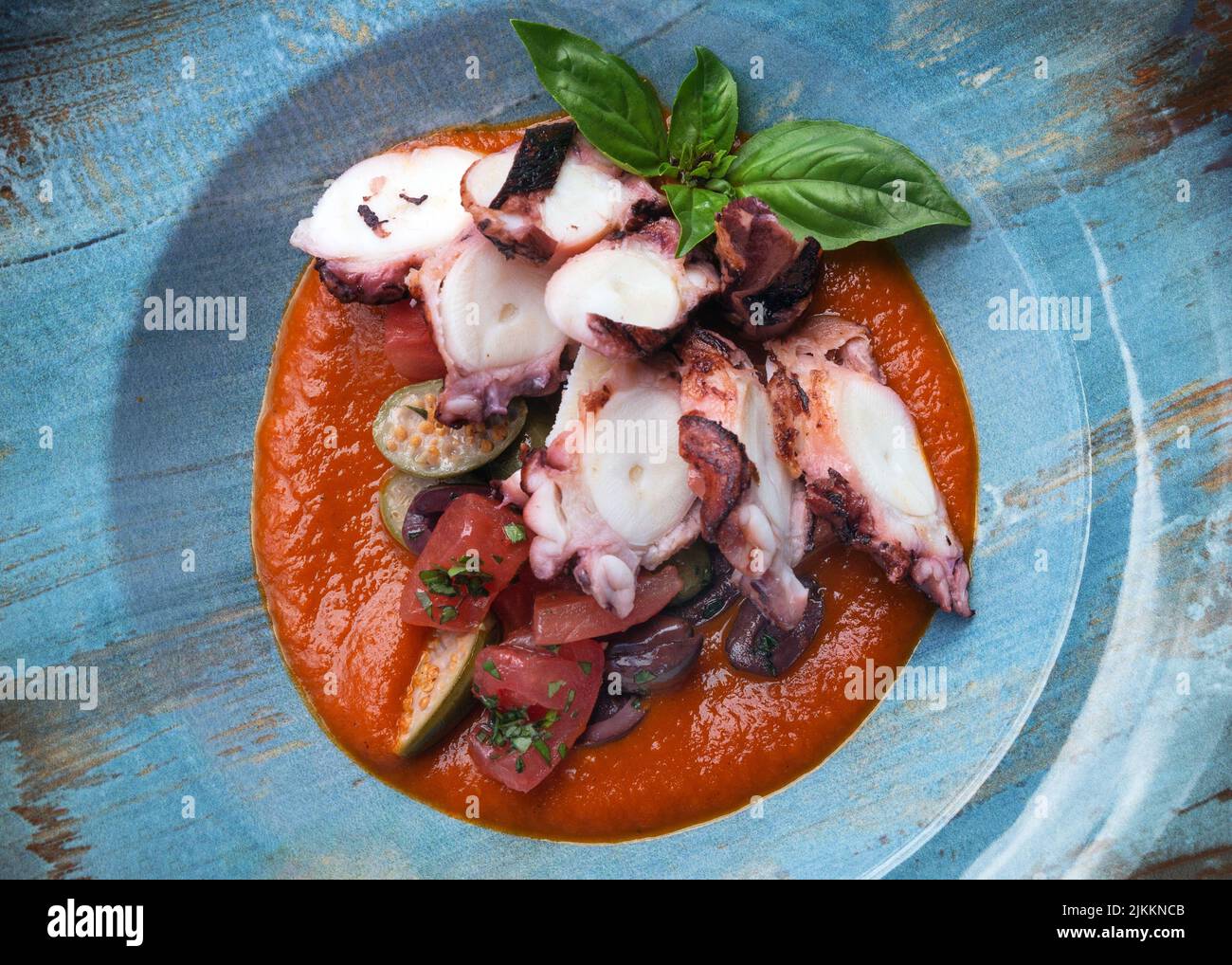 Fried octopus in tomato sauce with olives and capers in a blue plate