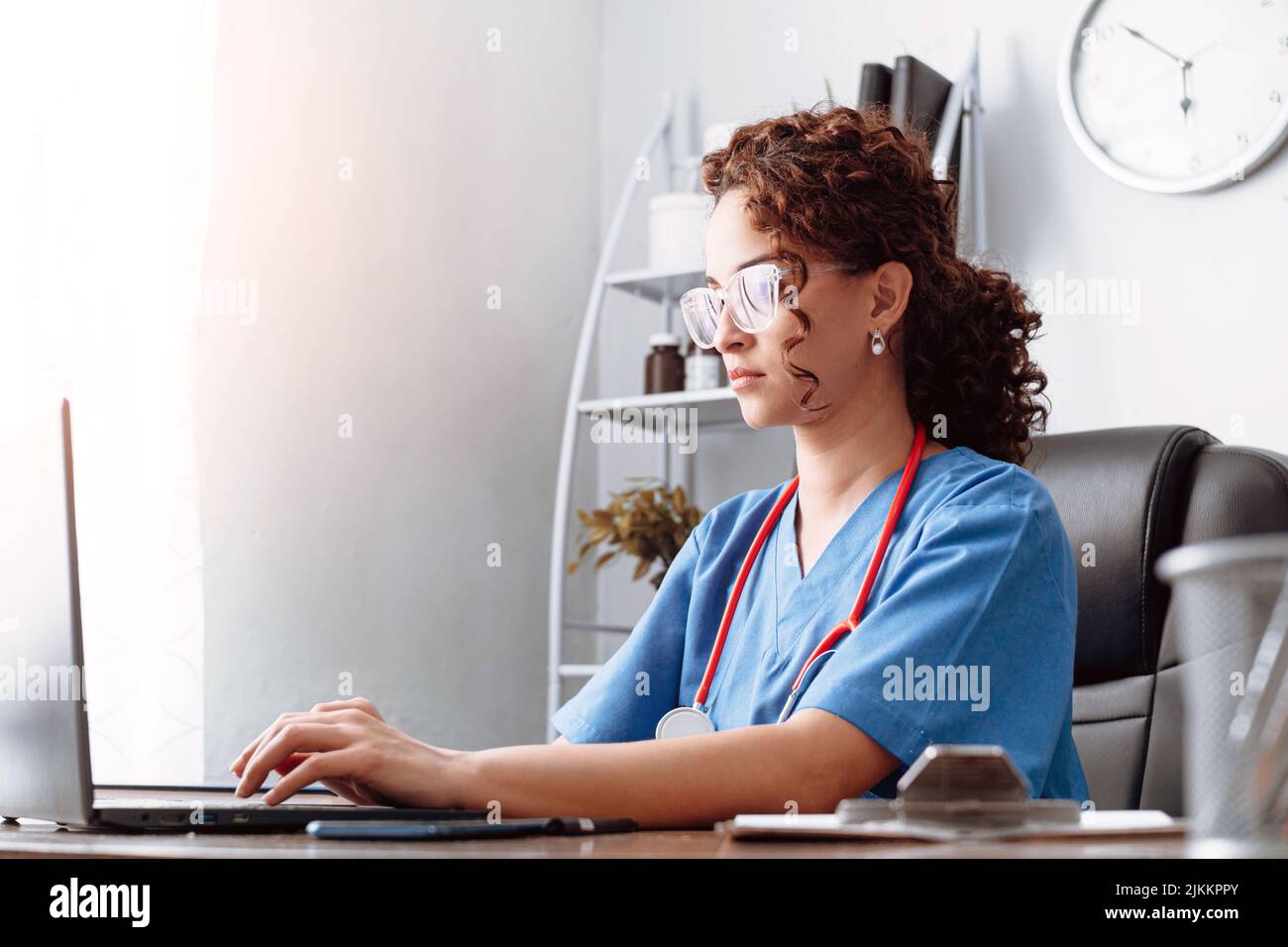Young hispanic woman wearing health uniform using a laptop. Stock Photo