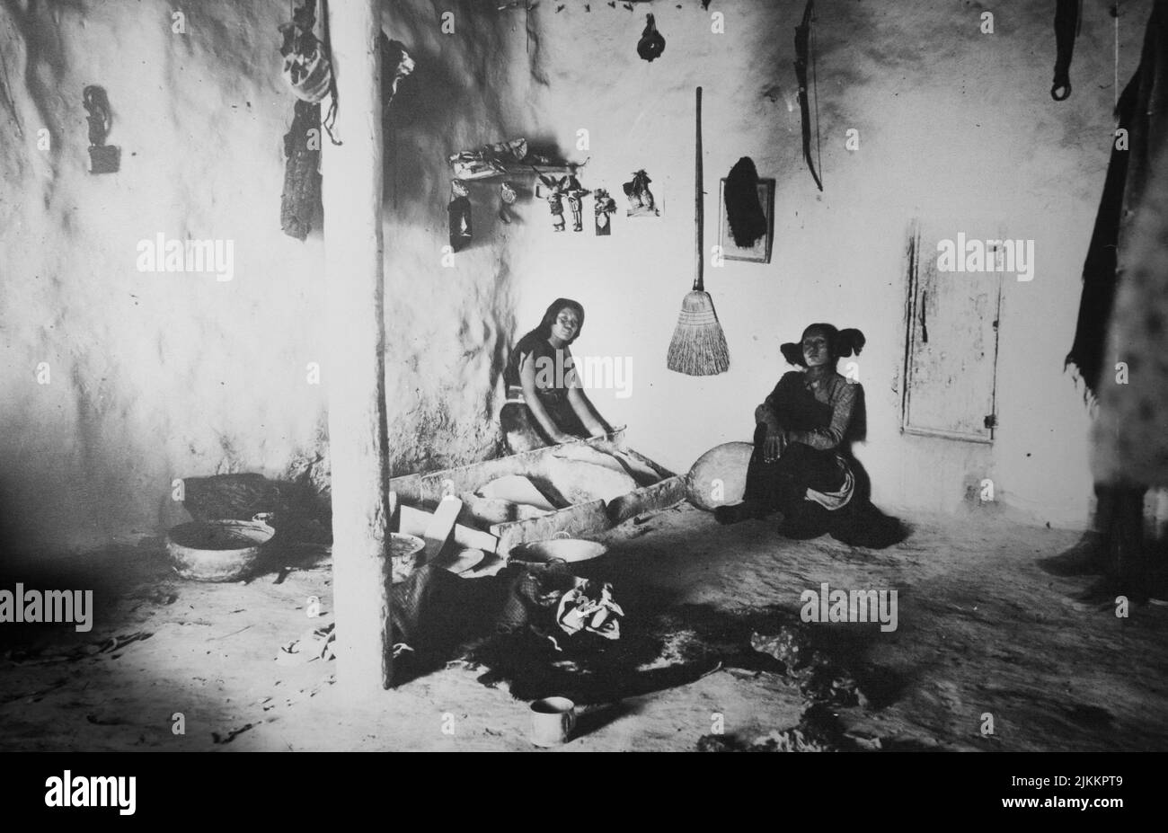 Black and white historical photograph of two Pueblo women inside a traditional adobe brick house with kitchen Stock Photo