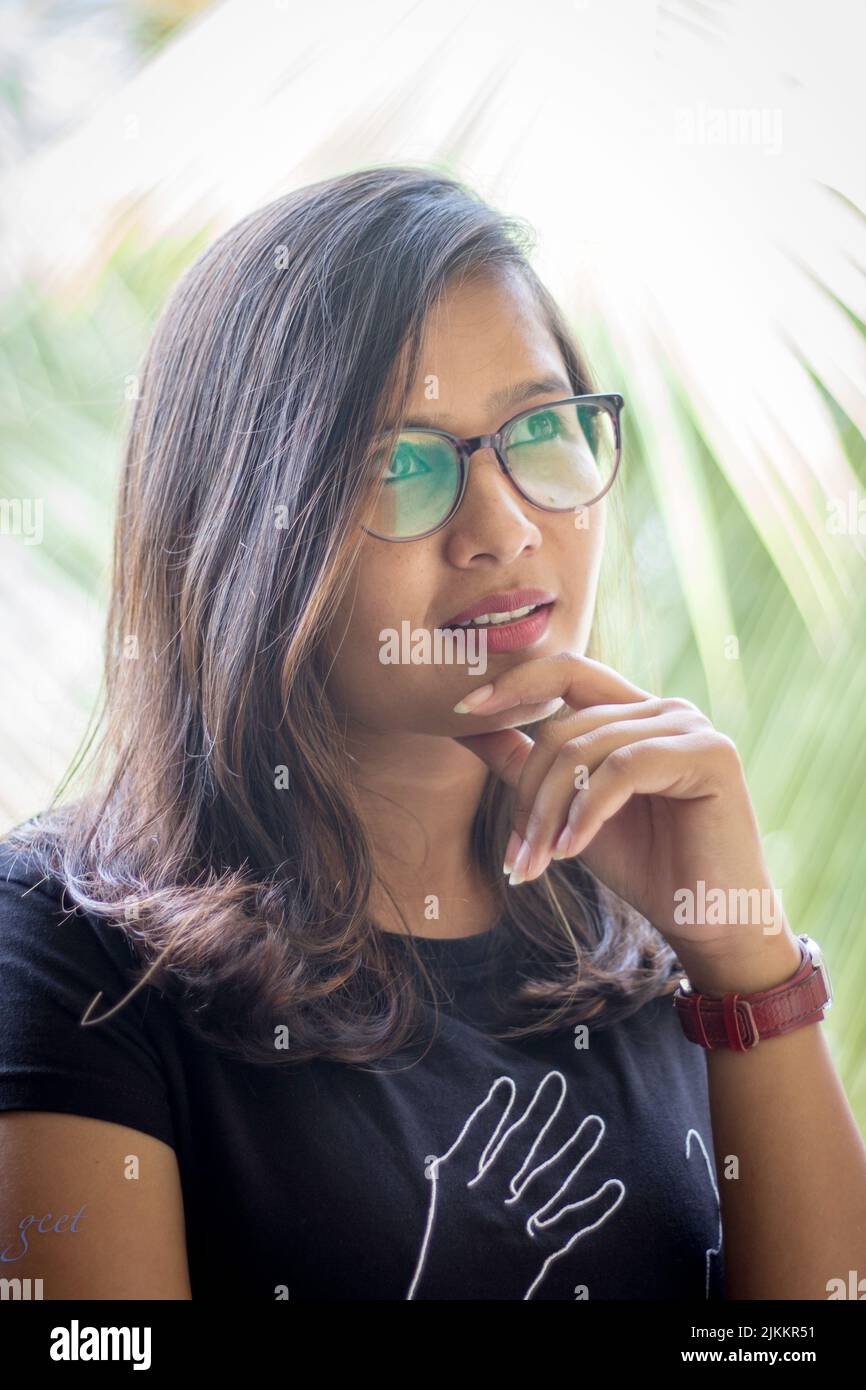 A vertical shot of a beautiful Indian woman wearing glasses and posing while pondering Stock Photo