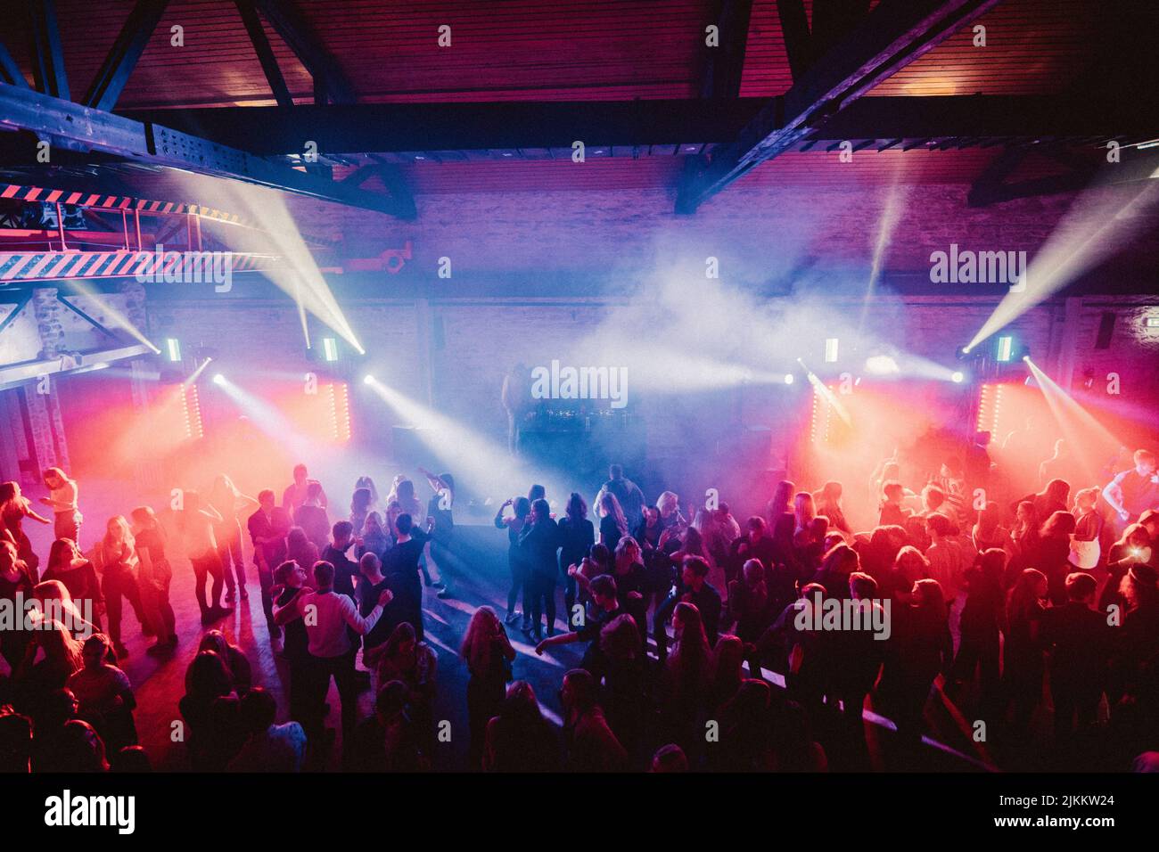 A group of people enjoying their time at a party with colorful lights in a warehouse Stock Photo