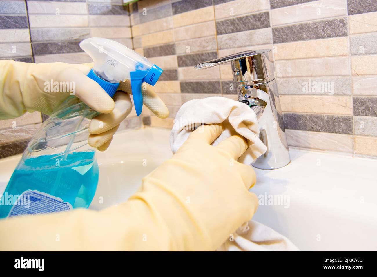 Hand cleaning a bath sink with a rag and sprayer with white gloves