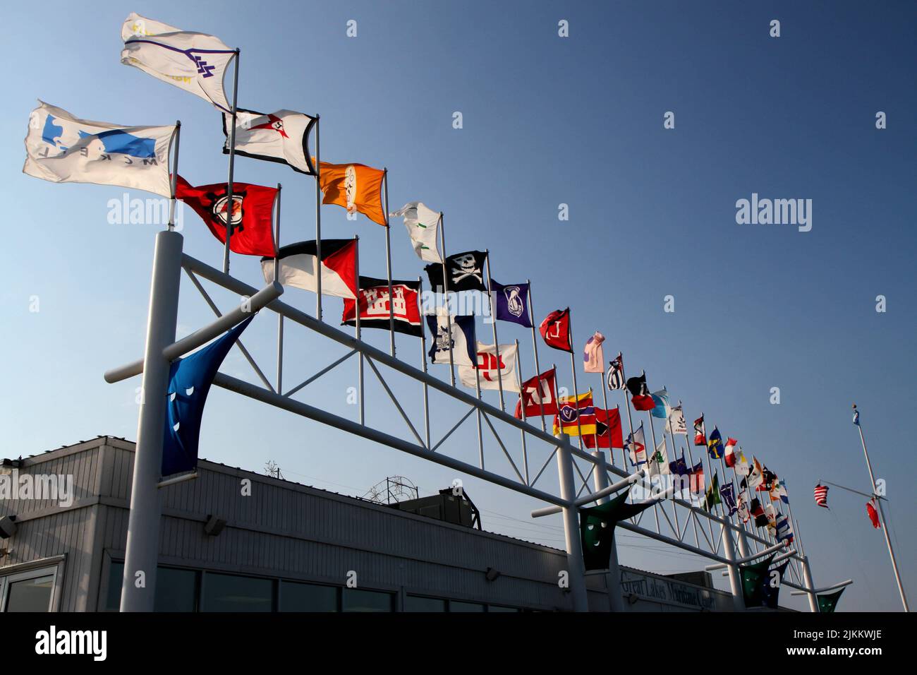 Flags of different countries waving on flagpoles against a blue sky at