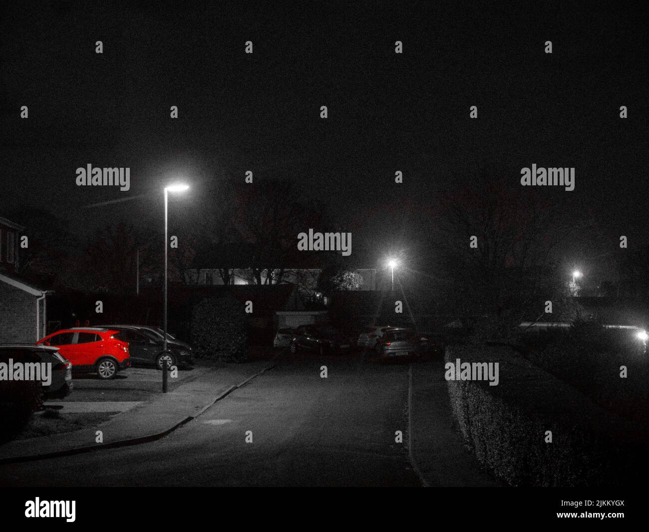 A grayscale view of a neighborhood with a single vibrant red parked car Stock Photo