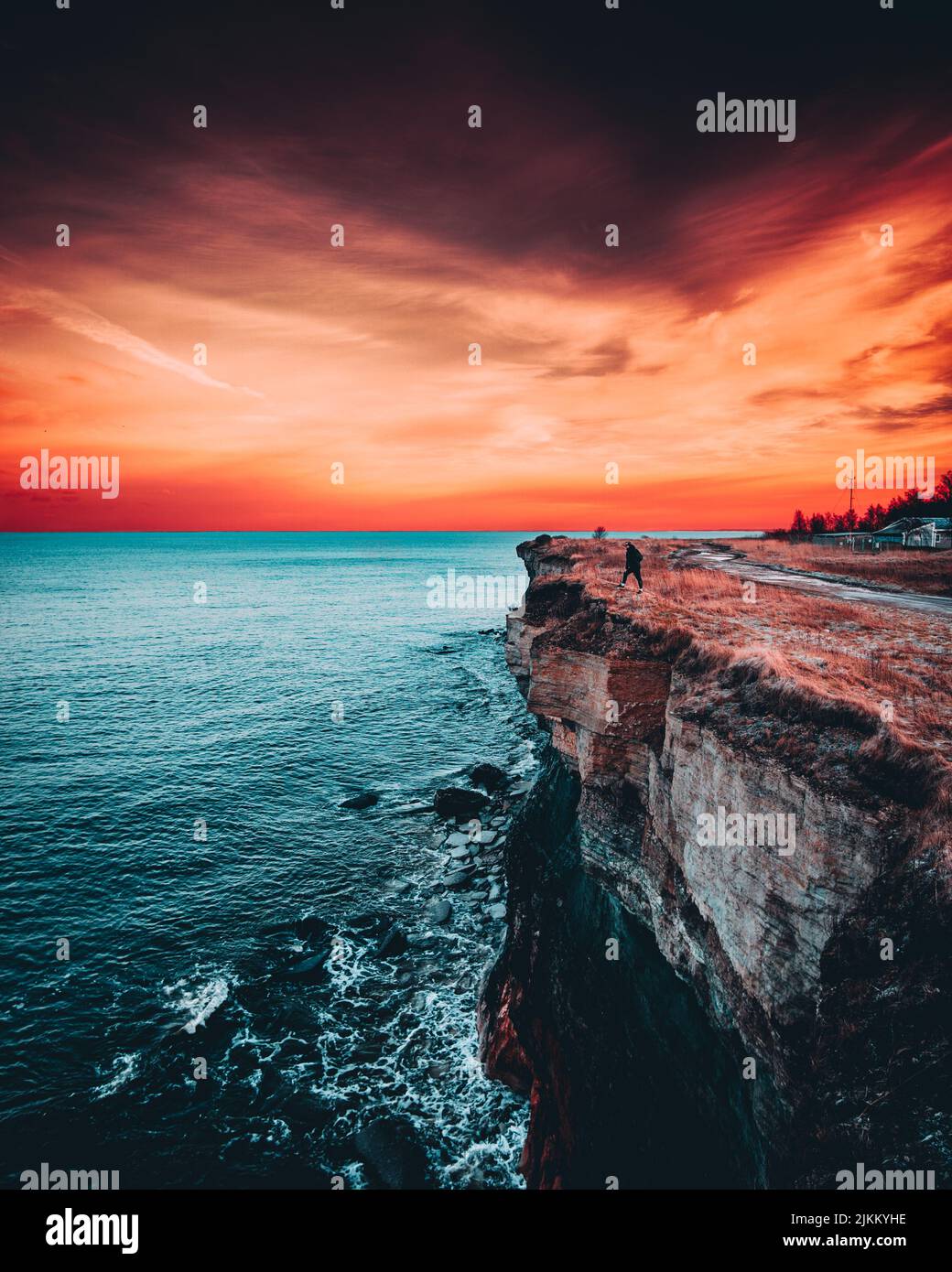 A vertical shot of a man on the edge of a cliff near the sea with
