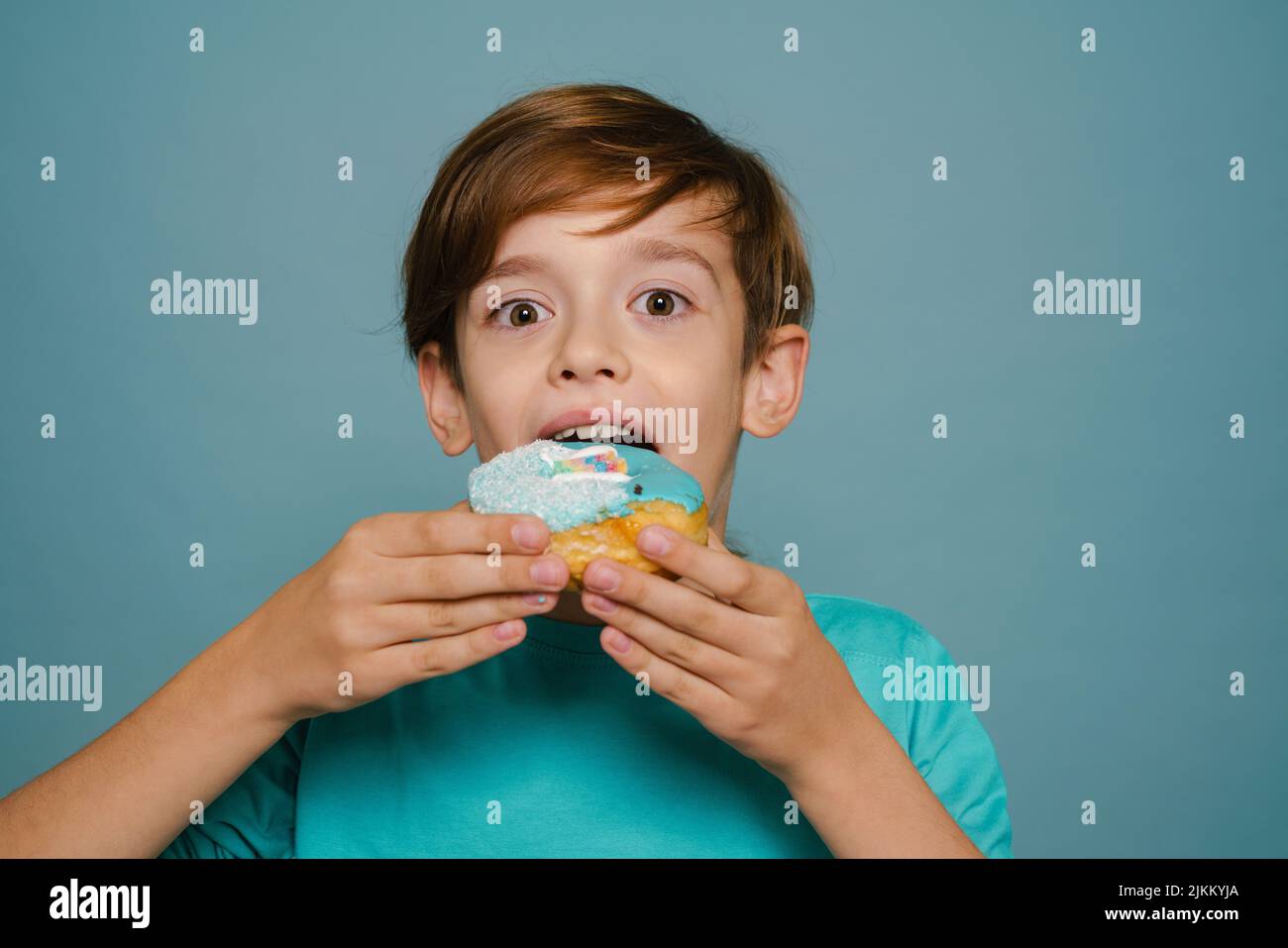 Ginger white boy wearing long sleeve eating doughnut isolated over blue