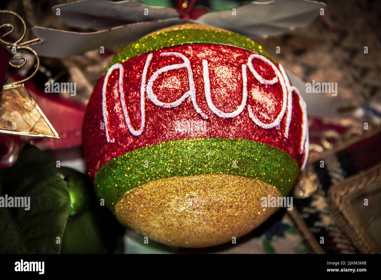 Close-up of Christmas ornament with glitter stripes reading NAUGHTY against Bokeh background Stock Photo
