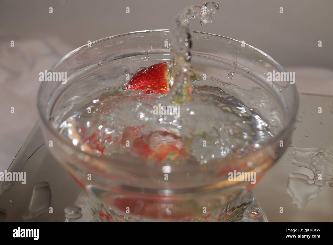A close-up shot of a strawberry falling into a bowl filled with water ...