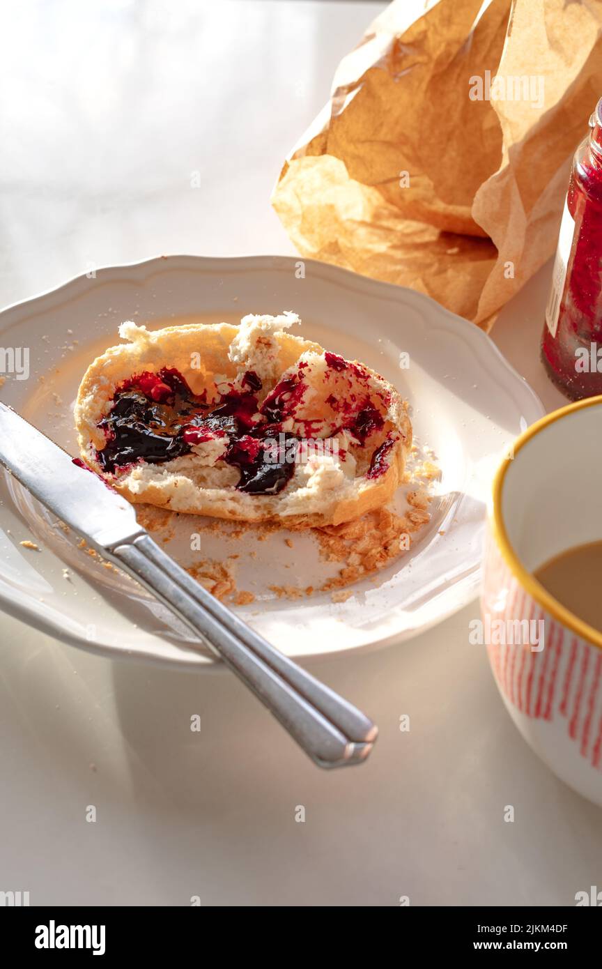 A vertical shot of a cut bread bun with jam on a plate for breakfast. Stock Photo