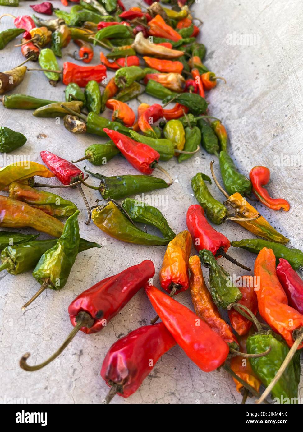 A vertical shot of drying green and red chili peppers on a stone ...
