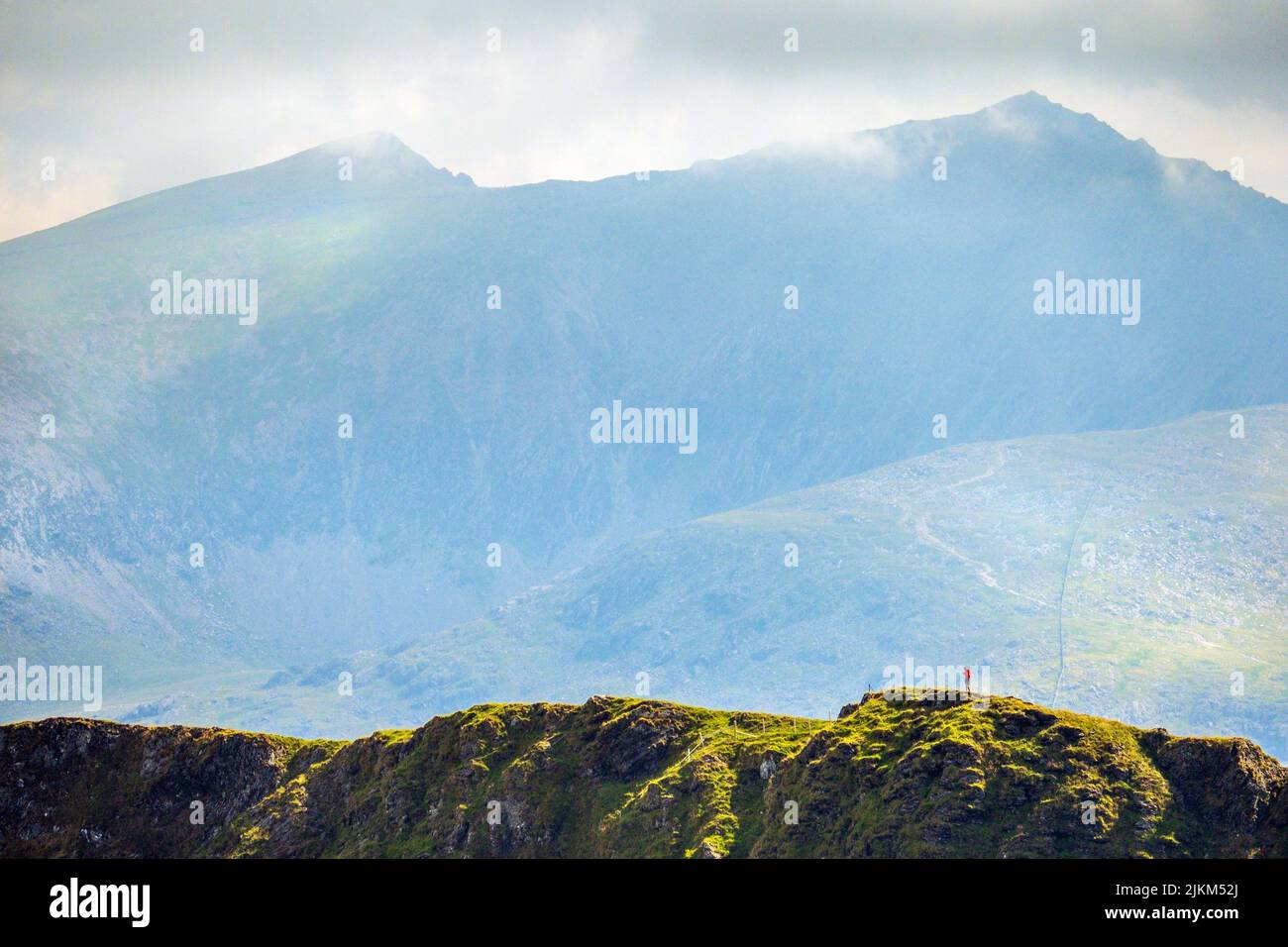 A walker on The Nantlle Ridge, a mountain ridge walk in Snowdonia, North Wales, UK. Snowdon is the peak in the distance Stock Photo