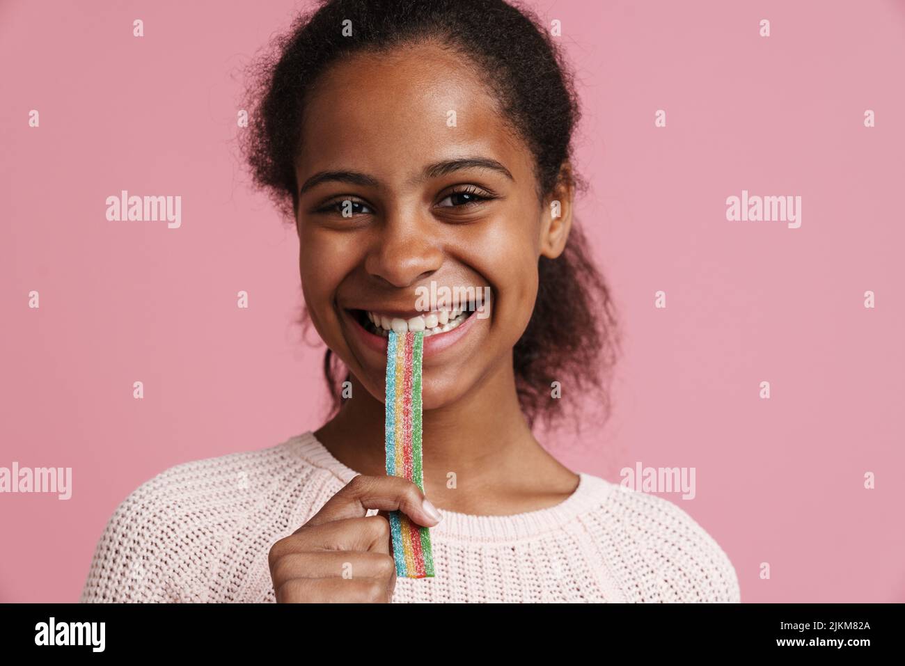 black girl smiling while eating candy worm isolated over pink