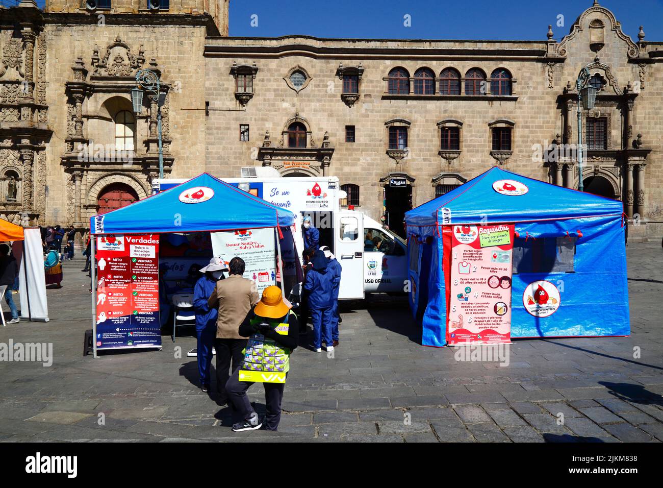 Plaza San Francisco, La Paz, Bolivia. 2nd August 2022. A doctor talks to a member of the public next to mobile collection centre where people can give blood, a service organised by the La Paz city health authorities. Bolivia's blood banks rely heavily on donations from volunteers and collection centres like this are common in the city, especially during holiday periods or when there are shortages. Behind is San Francisco church, the most important and impressive colonial church in the city. Stock Photo