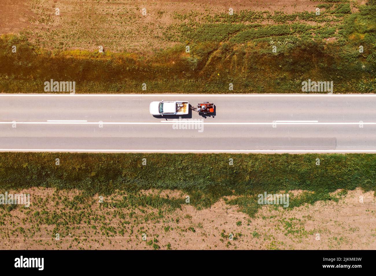 Aerial shot of pickup truck with trailer on highway through countryside landscape, drone pov directly above Stock Photo