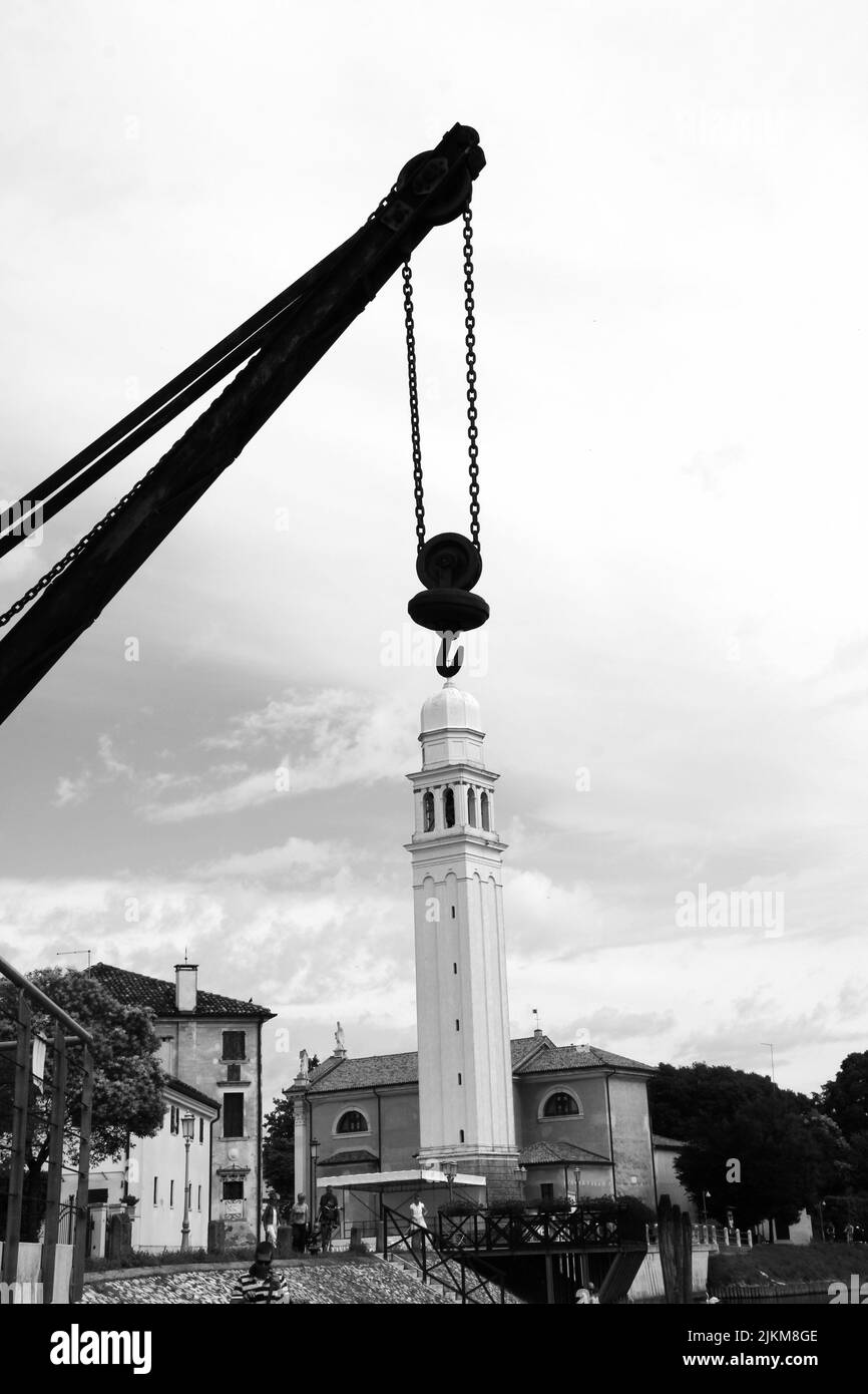 A grayscale shot of an industrial crane hook with the background of a bell tower Stock Photo
