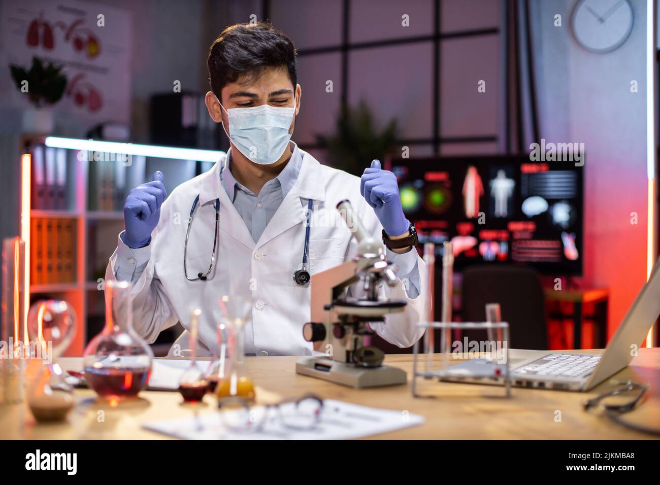 Indian male doctor microbiologist using microscope with vacuum tubes for samples with COVID 19 infection atypical pneumonia virus in laboratory. Stock Photo