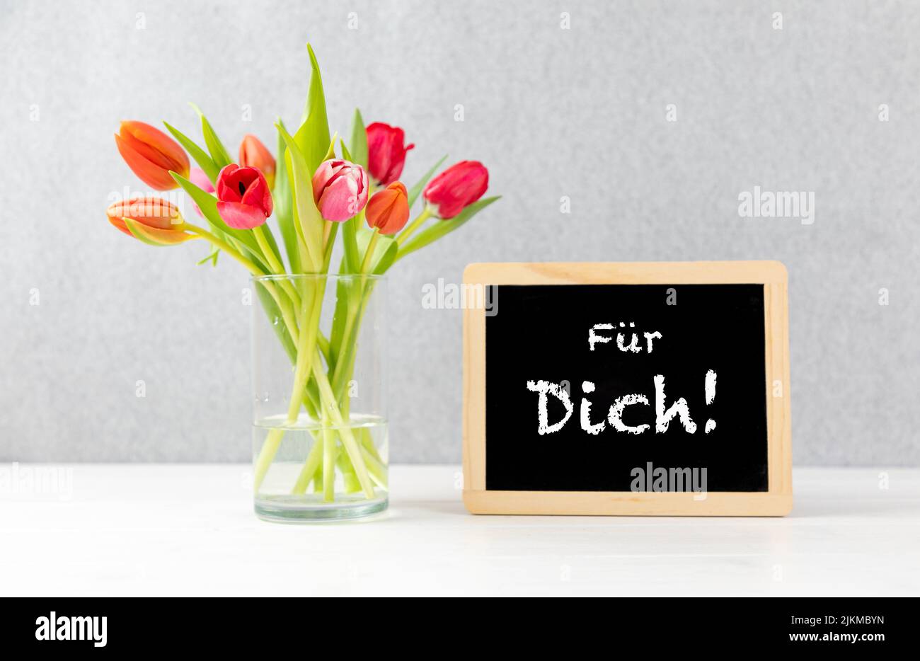 colorful tulips in a Vase with gray background and chalkboard with german text für dich, in english for you Stock Photo