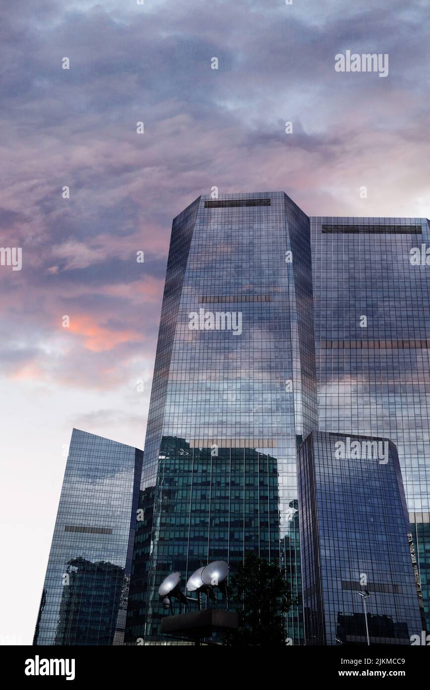 A vertical shot of a beautiful high- rise glass building at the sunset ...