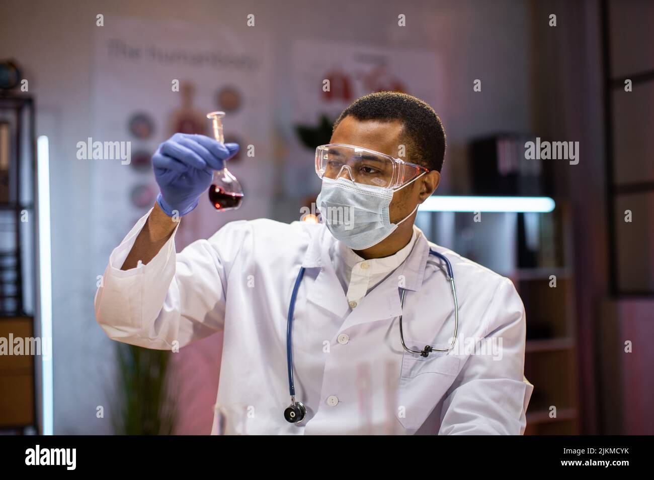 African american male doctor microbiologist using microscope with vacuum tubes for samples with COVID 19 infection atypical pneumonia virus in laboratory. Stock Photo