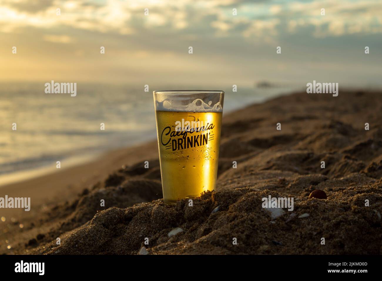 A shallow focus shot of a California Drinkin Beer cup on the Huntington Beach Sand, USA with sunset sky on the horizon Stock Photo