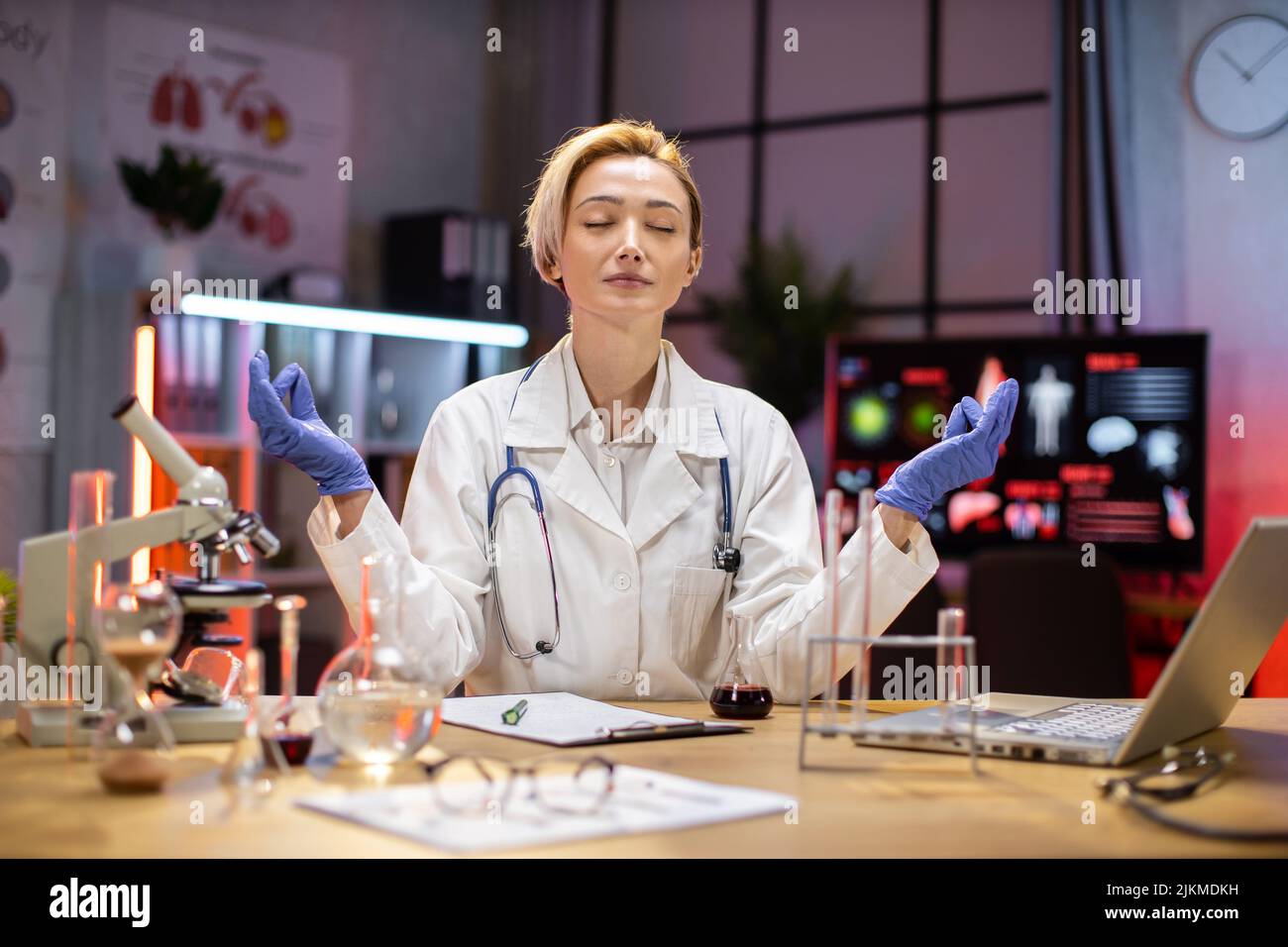 Yong female scientist relaxing practicing yoga wearing lab coat working