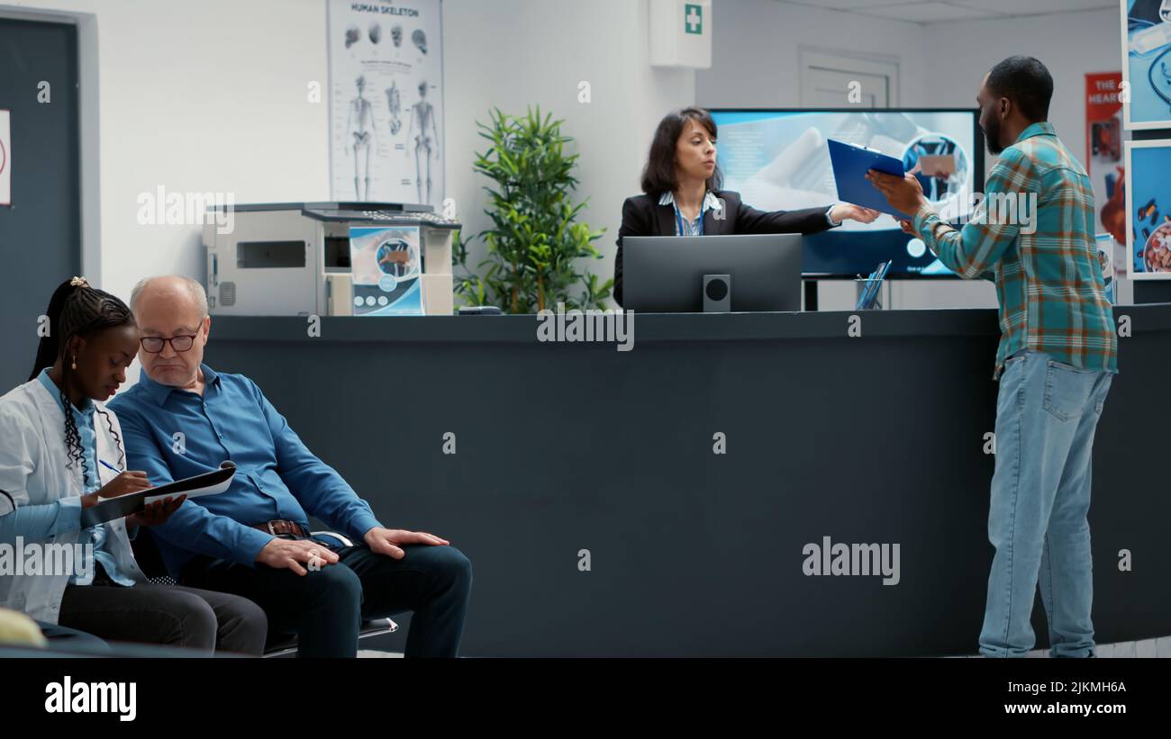 Female receptionist helping patients to fill in medical report for ...