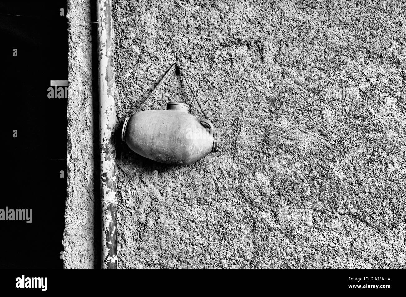 A grayscale shot of a small ancient artifact hanging with a rope on an old wall Stock Photo