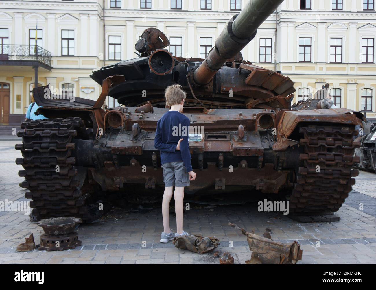 Kiev, Ukraine. 08-02-2022. A skinny boy looks at a burnt-out Russian tank during the Russian-Ukrainian conflict. The remains of a rusty military vehic Stock Photo