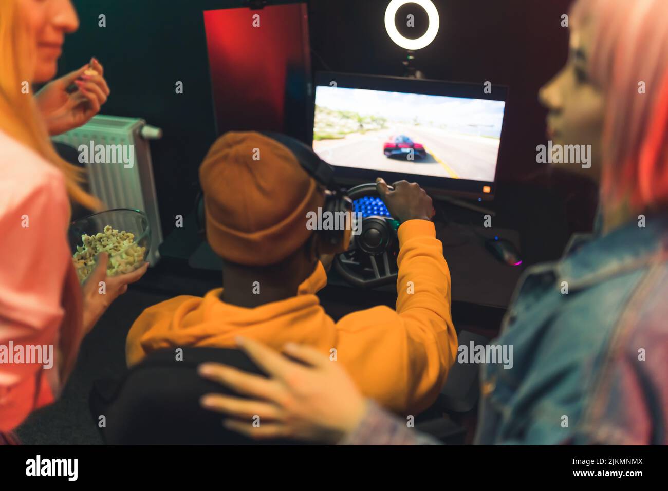 Two teenage girls talking watching teenage boy playing racing game