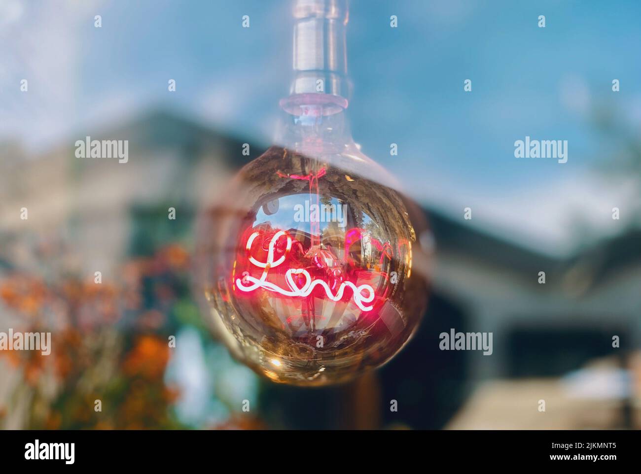 A shallow focus shot of a lightbulb with neon 'love' writing in it behind a glass window Stock Photo