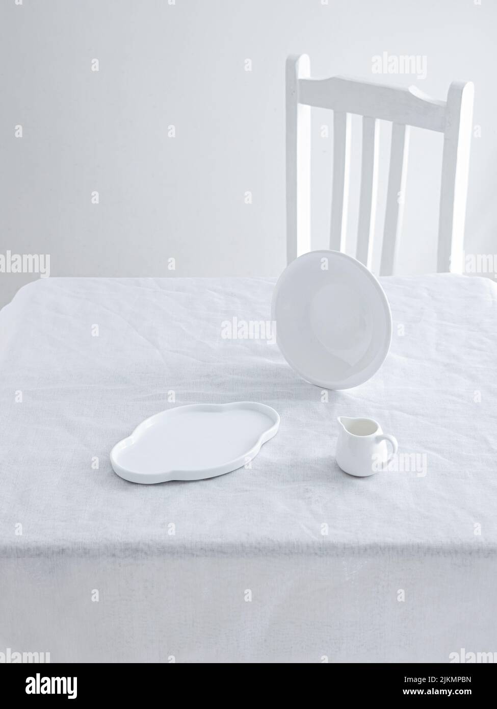 A small coffee cup and plates on a table and a chair on a white