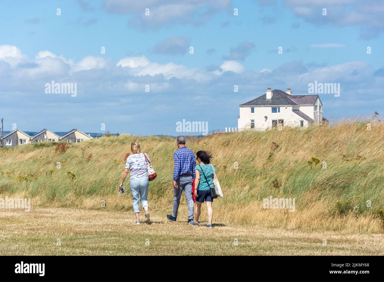 Group walking past sand dunes, Amble, Northumberland, England, United Kingdom Stock Photo