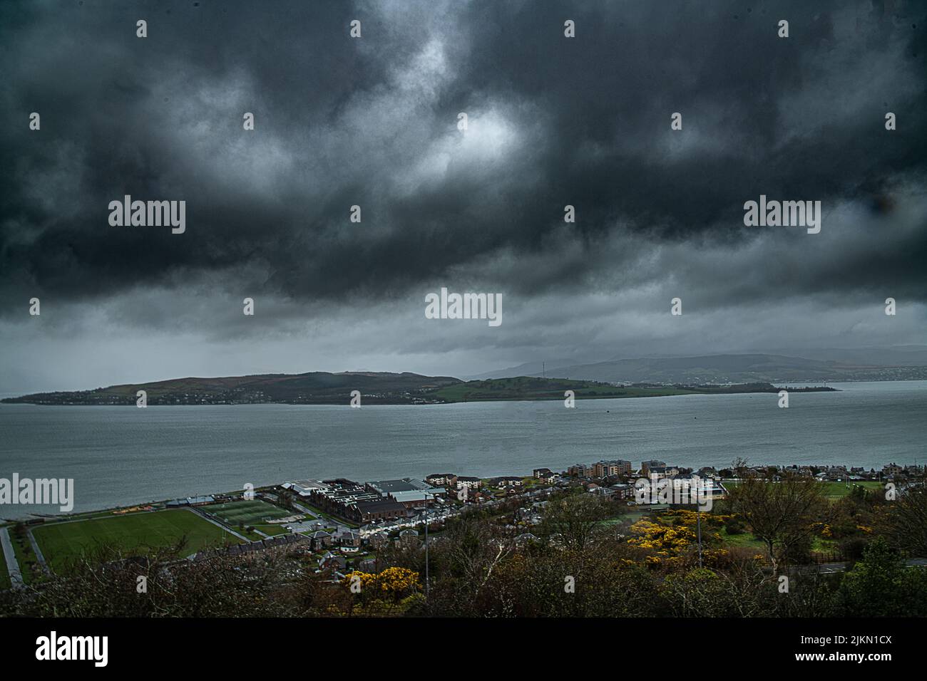 A scenic view of the seashore by the tranquil water under the stormy sky Stock Photo