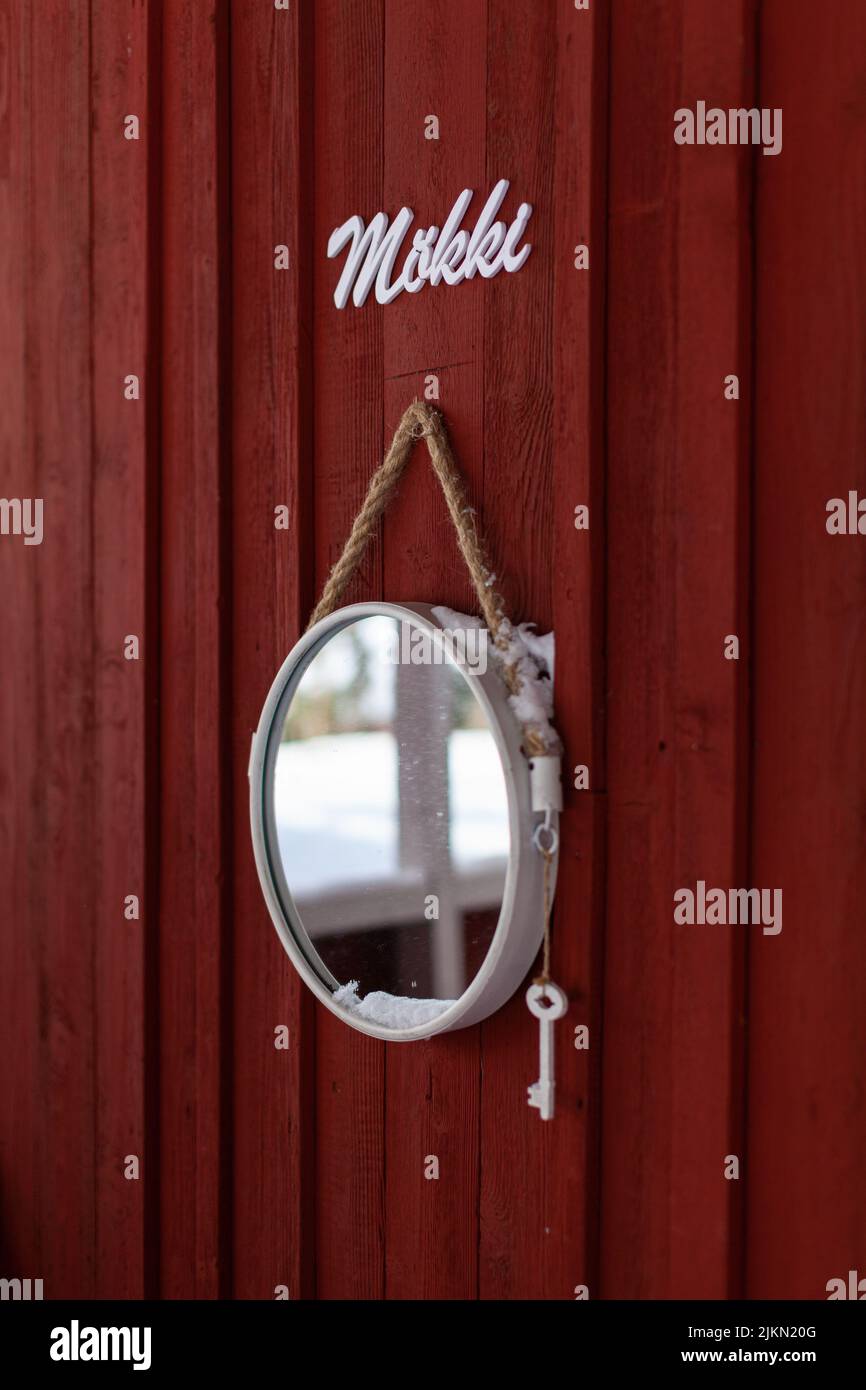 A vertical shot of a hanging, small, circle shaped mirror on a background of a red, wooden wall Stock Photo