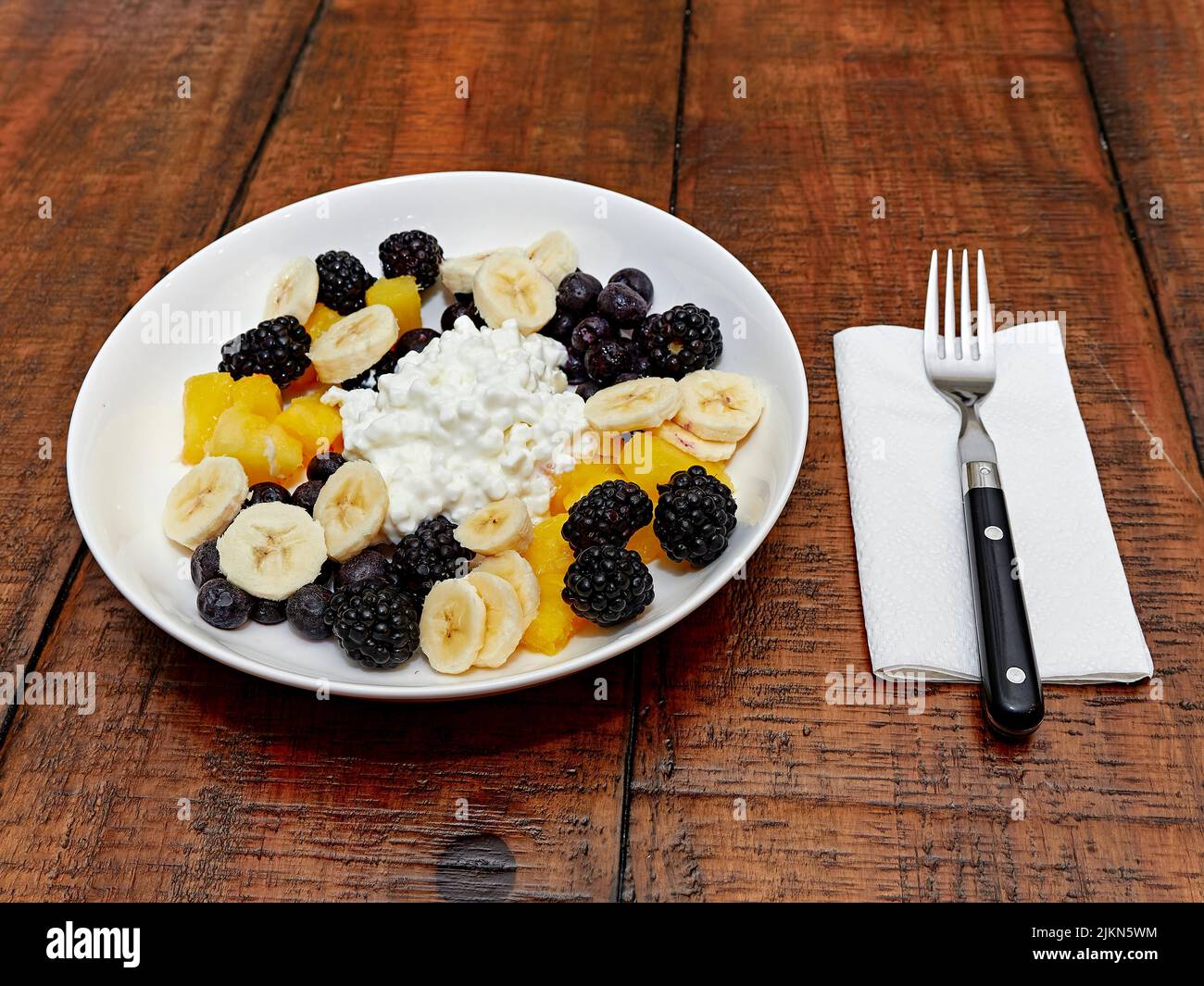 Healthy meal for breakfast or lunch bowl of cottage cheese and fruit consisting of banana slices, blueberries and blackberries, overhead view. Stock Photo