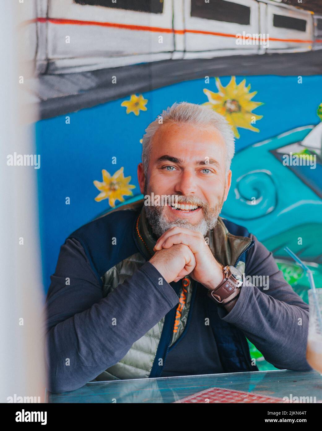 A vertical shot of a handsome adult with gray hair and blue eyes sitting happily in a cafe Stock Photo